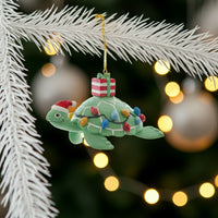Decorative turtle ornament with Christmas lights and a present on a tree branch with blurred lights in the background.