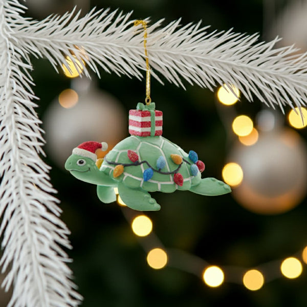 Decorative turtle ornament with Christmas lights and a present on a tree branch with blurred lights in the background.