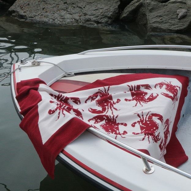 A red and white cotton throw blanket by In2Green with crab patterns displayed on a wooden ladder.