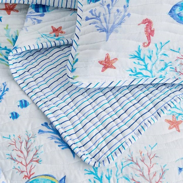 A coastal seascape-designed lightweight quilt set for a bed, with a pattern of marine life including fish and coral in blue and white tones.