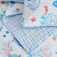 A coastal seascape-designed lightweight quilt set for a bed, with a pattern of marine life including fish and coral in blue and white tones.