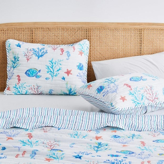 A coastal seascape-designed lightweight quilt set for a bed, with a pattern of marine life including fish and coral in blue and white tones.