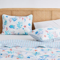 A coastal seascape-designed lightweight quilt set for a bed, with a pattern of marine life including fish and coral in blue and white tones.