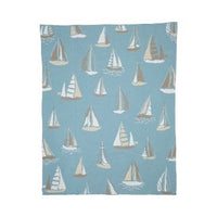 A rectangular light blue throw cotton blanket by In2Green with a nautical sailboat pattern.