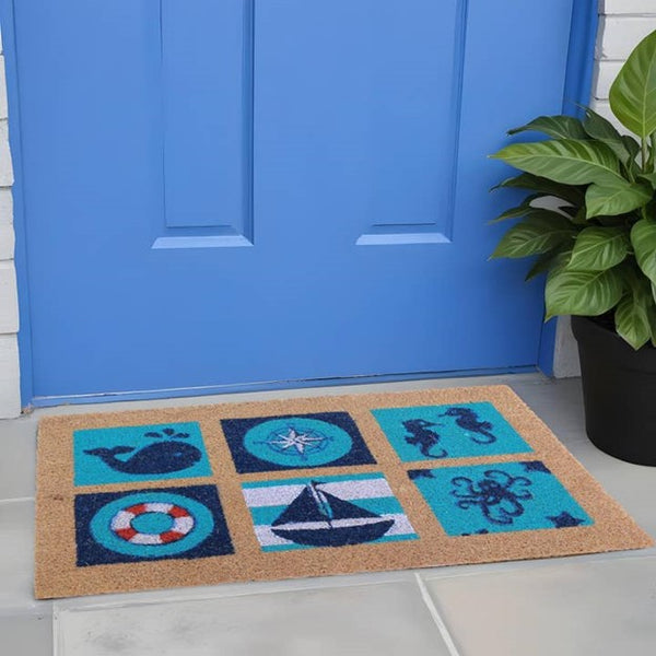 A rectangular coir outdoor door mat with nautical designs including a whale, a lifebuoy, and a sailboat, placed on a doorstep.