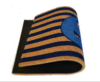 A coir door mat with blue stripes and a central anchor design, placed on a doorstep.