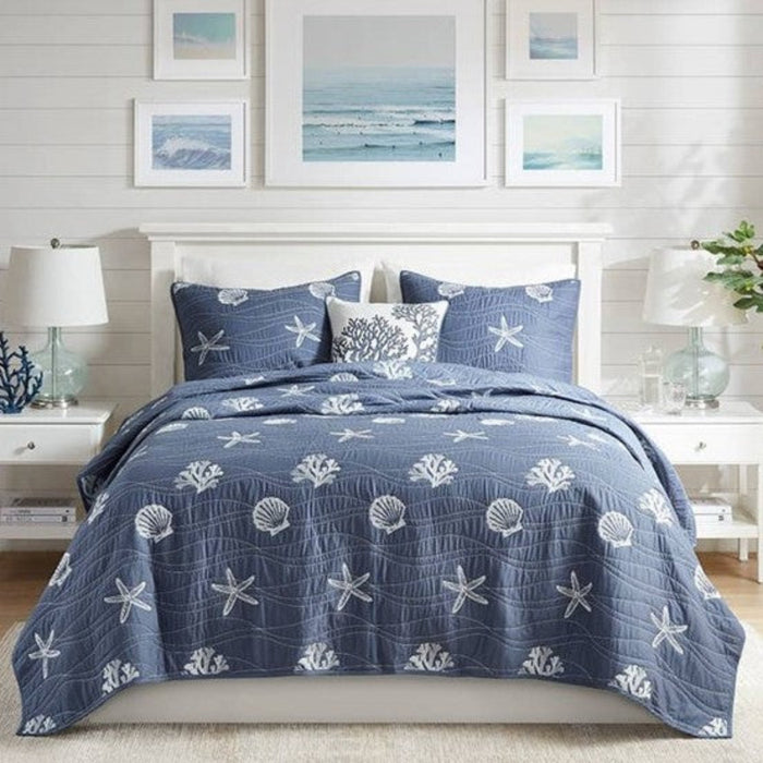 Nautical-themed bedding set with starfish and shell patterns on a bed in a bedroom setting.