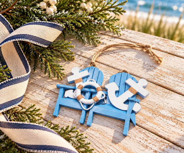 A nautical-themed wooden hanging ornament shaped like two blue chairs with white anchors and a small white life preserver, styled on a weathered wooden surface with a navy-and-cream ribbon and evergreen branches.
