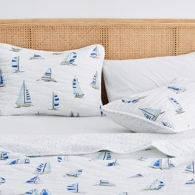 Bed with a white quilt with a nautical blue sailboat patterned bedding and mathcing pillows in a bright room.