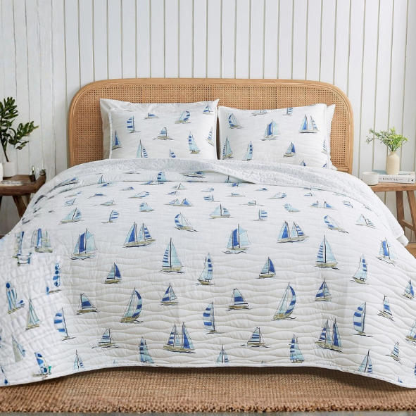 Bed with sailboat patterned bedding in a room with striped walls and wooden floors.