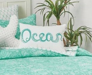 A rectangular throw pillow with the word 'ocean' written in a stylized font, where each letter is replaced with an embroidered octopus tentacle design in turquoise color on a white background.