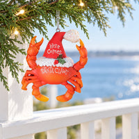 Santa Claws red ceramic Christmas Ornament with Santa hat hanging from Christmas branch overlooking water.