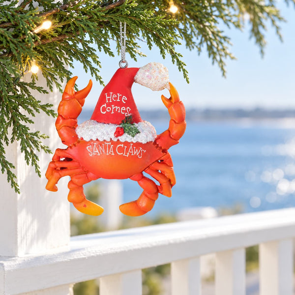 Santa Claws red ceramic Christmas Ornament with Santa hat hanging from Christmas branch overlooking water.