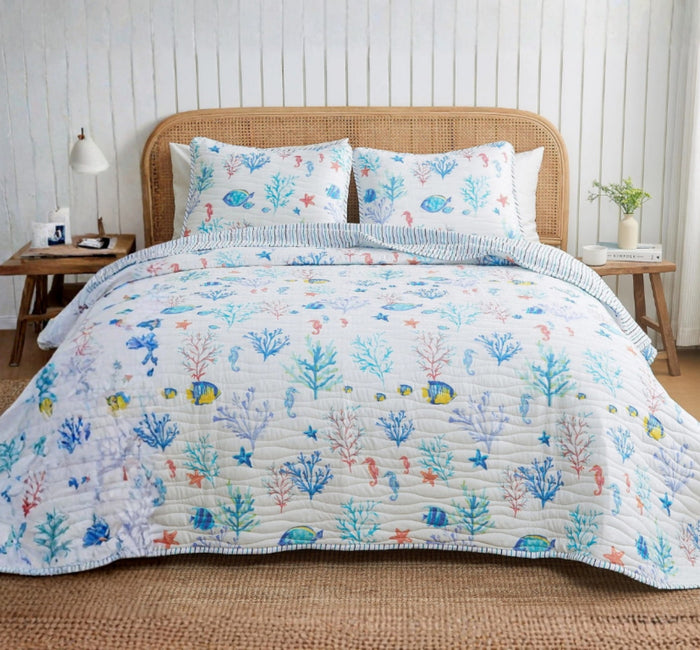 A coastal seascape-designed lightweight quilt set for a bed, with a pattern of marine life including fish and coral in blue and white tones.