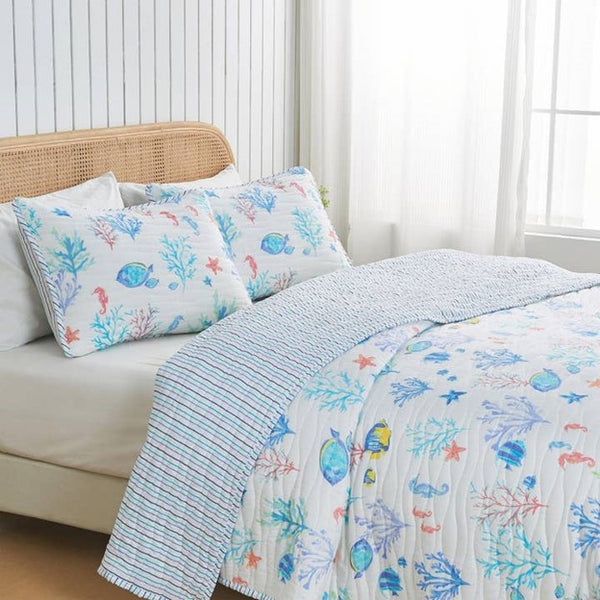 A coastal seascape-designed lightweight quilt set for a bed, with a pattern of marine life including fish and coral in blue and white tones.