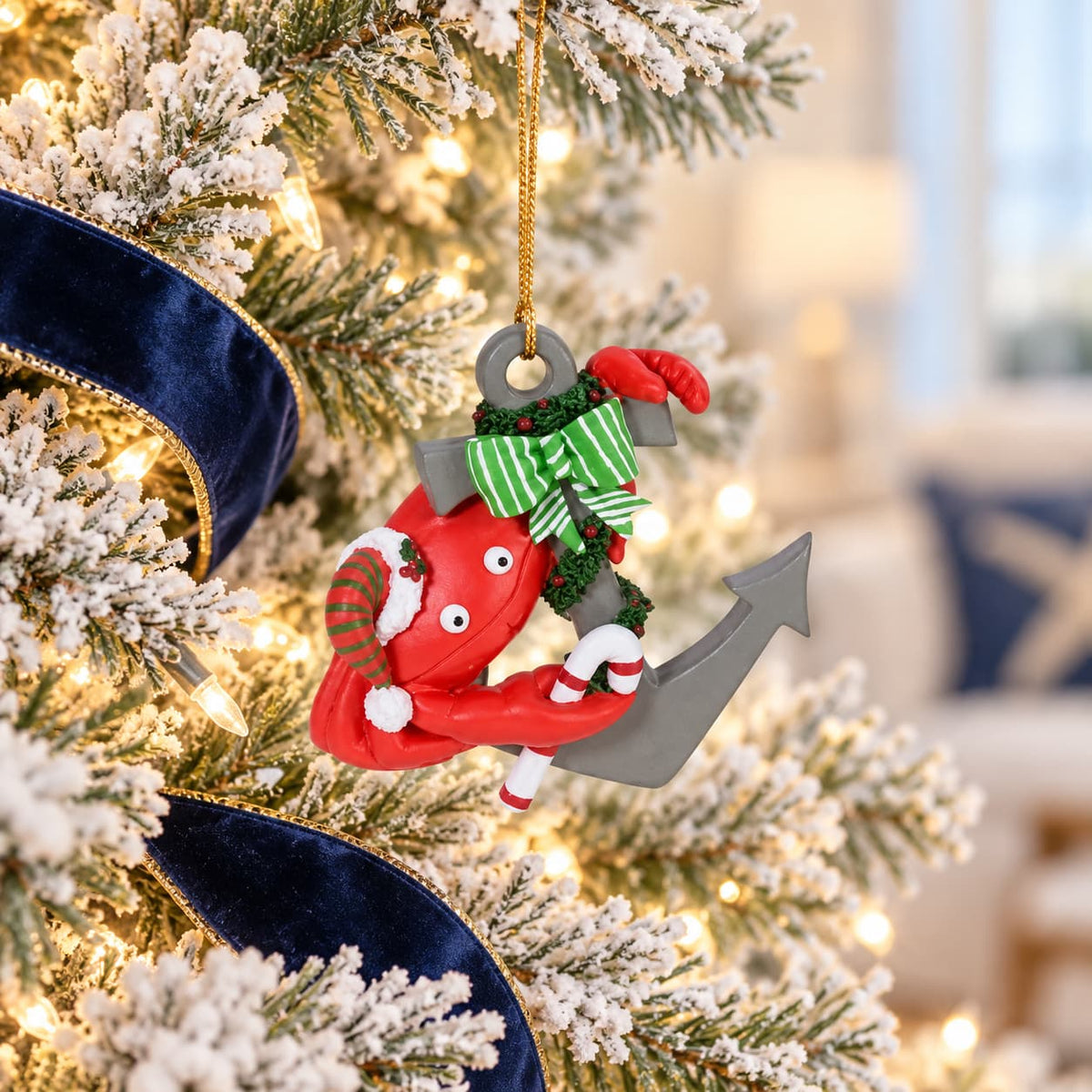 A Christmas ornament shaped like a red crab climbing an anchor, decorated with a green striped hat and red-and-white striped socks, hanging on a flocked Christmas tree with warm lights and a blue ribbon.