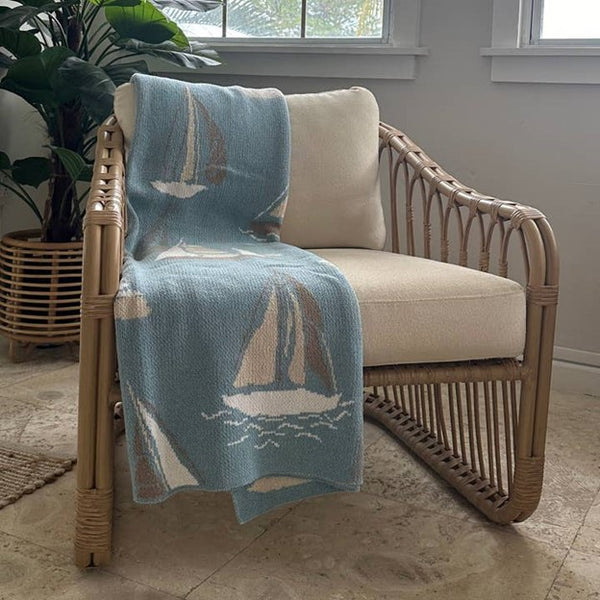 A rectangular light blue throw cotton blanket by In2Green with a nautical sailboat pattern.