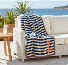 Navy and white striped blanket with an anchor design on a white outdoor sofa by the sea.