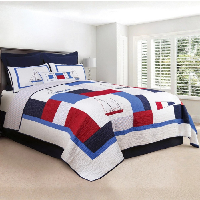 Nautical-themed sailboat quilt with red, white, and blue colors on a bed in a room.