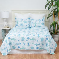 A bed with a blue quilt set featuring starfish and coral patterns, with two shams, placed in a room with a nightstand and a plant.
