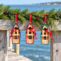 Blue, Red and Green Wooden Rowboat Ornaments hanging from a pine branch over the water