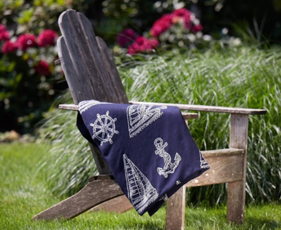 Navy blue blanket with white sailboat patterns draped over a wooden chair in a garden setting.