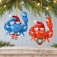Decorative and whimsical red and blue crab with sparkly Santa hats carrying a wreath and present Christmas Ornaments hanging from a pine branch