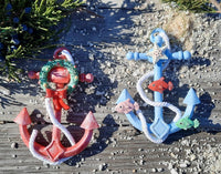 Two whimsical anchor Christmas ornaments, one red and one blue, with a wreath and fishes.