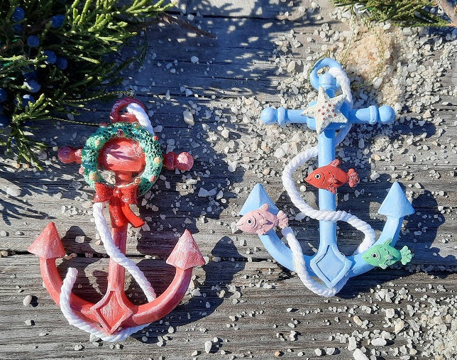 Two whimsical anchor Christmas ornaments, one red and one blue, with a wreath and fishes.